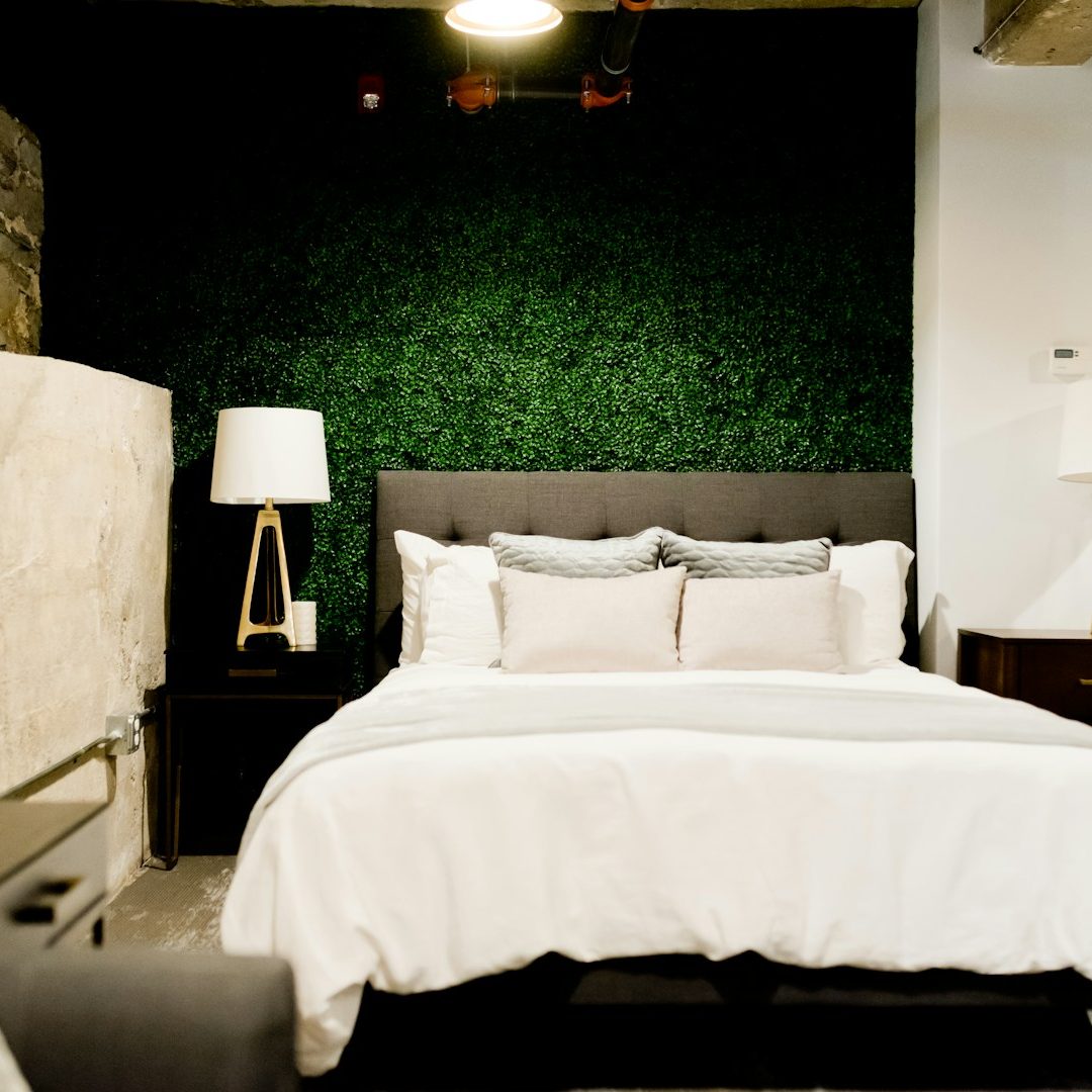 Lit de chambre avec oreillers blancs et lampe de chevet sur fond bleu-vert.