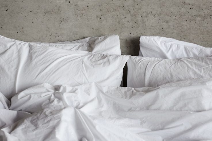 Draps blancs froissés avec des oreillers sur un lit au fond en béton.